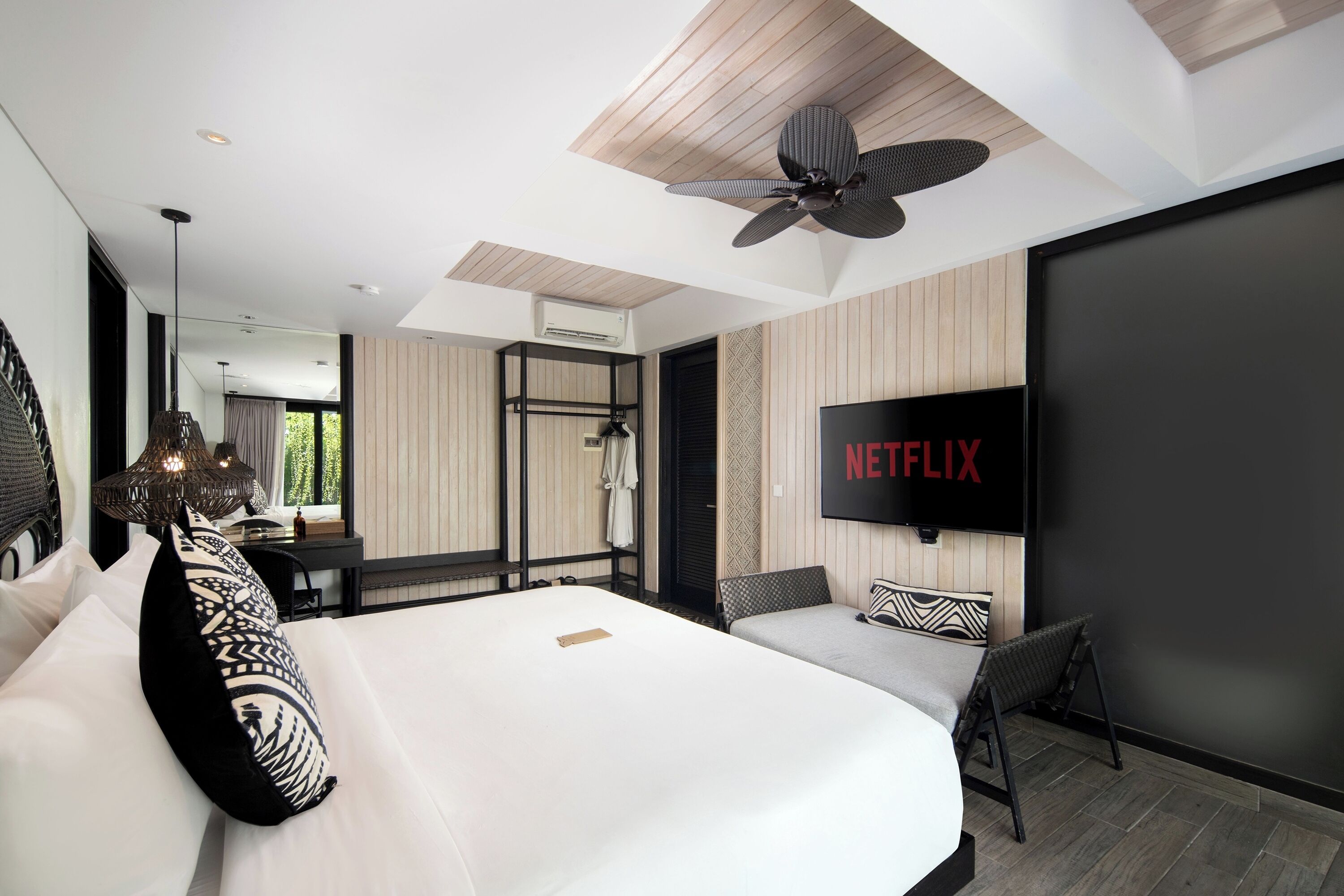 A modern hotel room with a large bed, a ceiling fan, a TV mounted on the wall, and a desk with a chair.