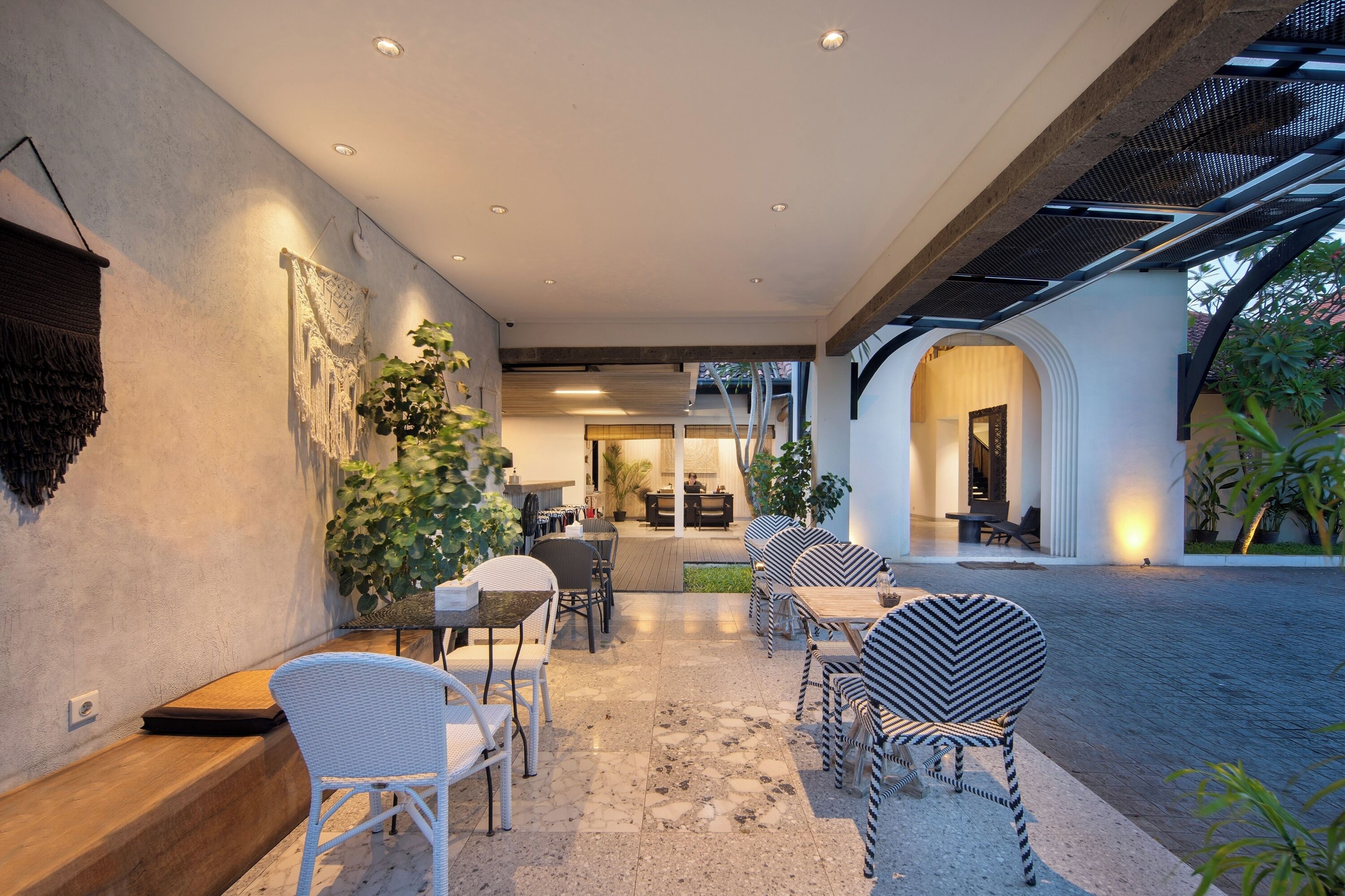 Un patio al aire libre con mobiliario de mimbre, un banco de madera y vista al interior a través de un arco.