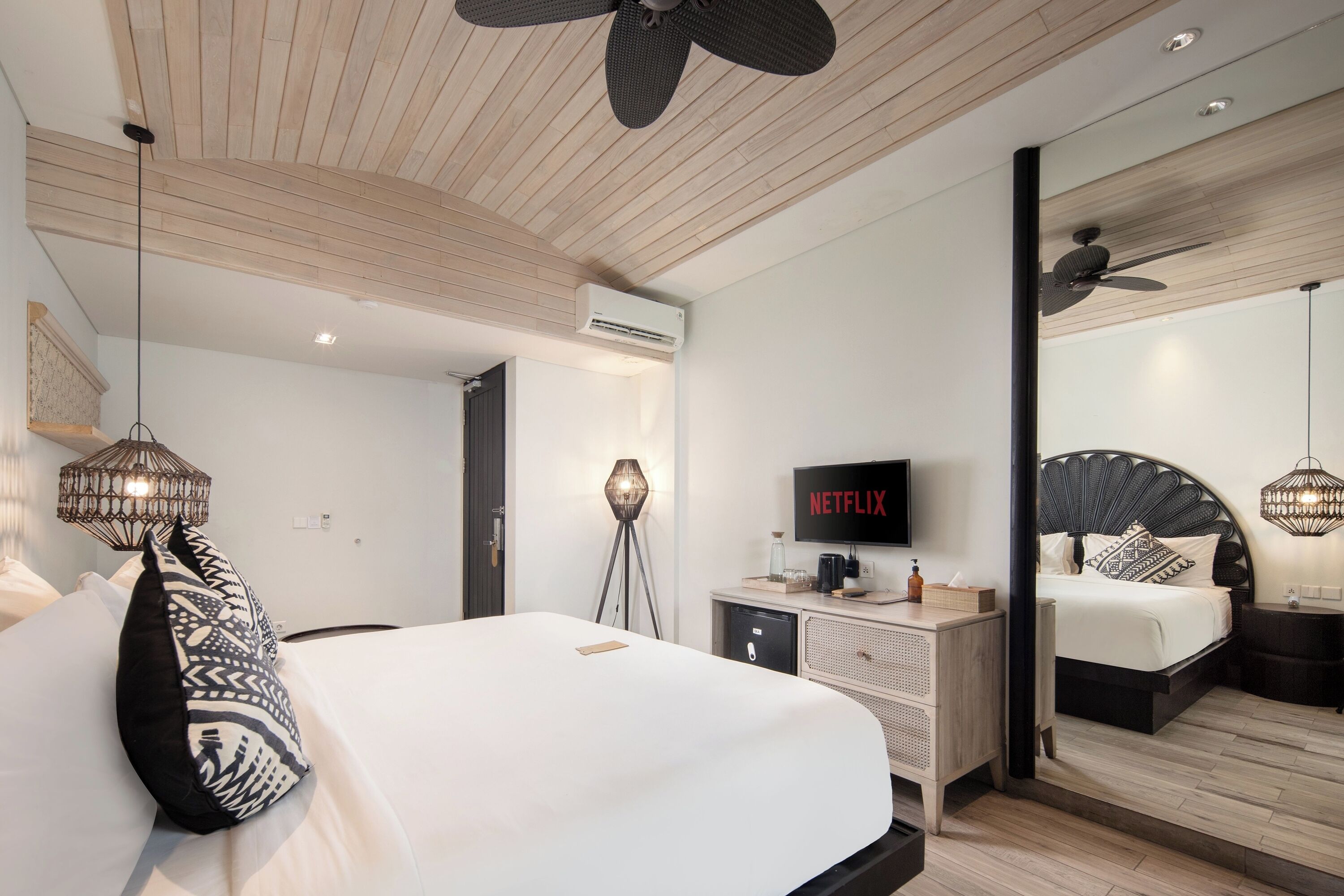 A modern bedroom with a large bed, a TV, a ceiling fan, and a nightstand.