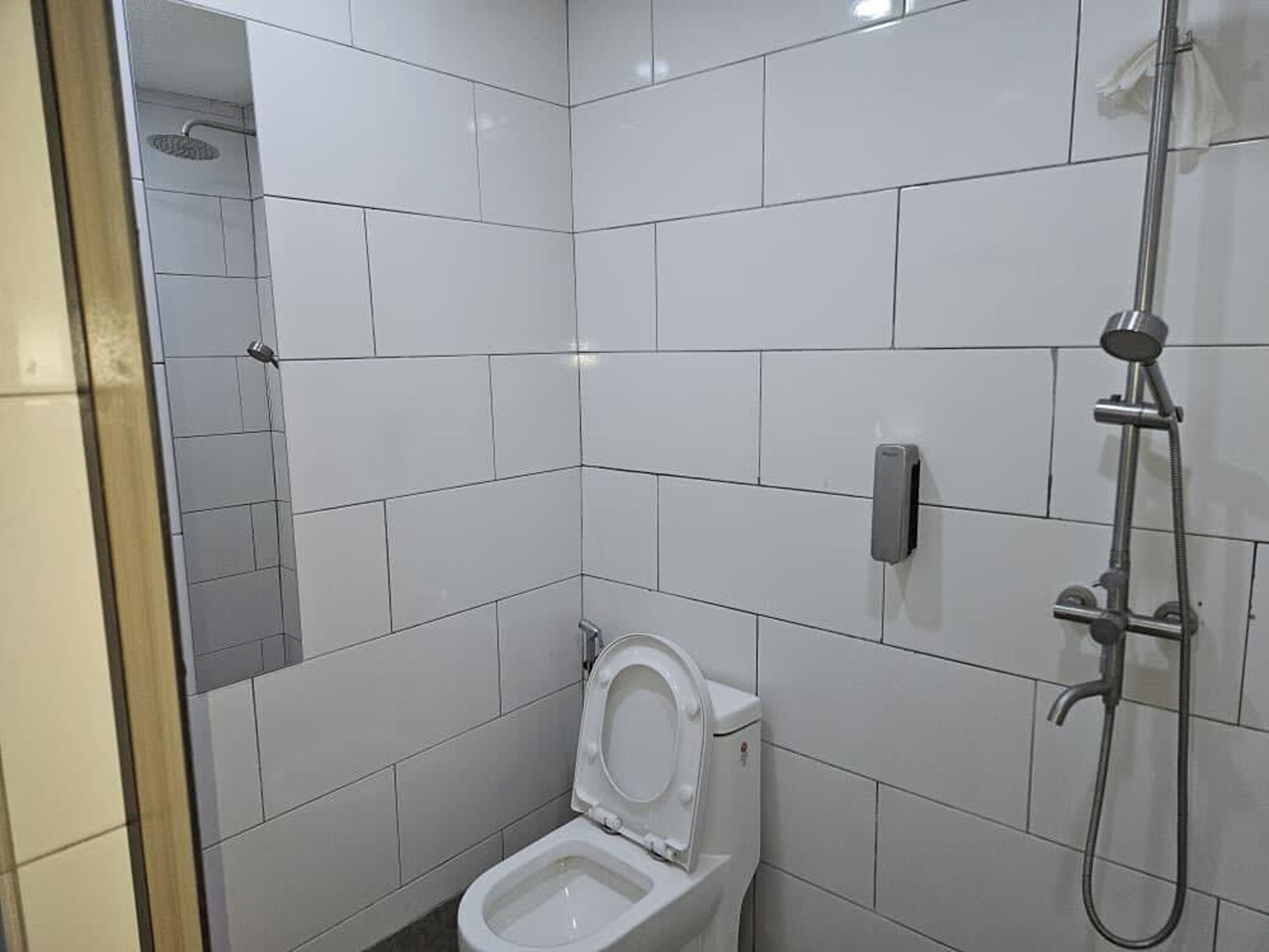 Pieni, siisti kylpyhuone, jossa on valkoiset laatat, wc-istuin, käsisuihku ja peili.