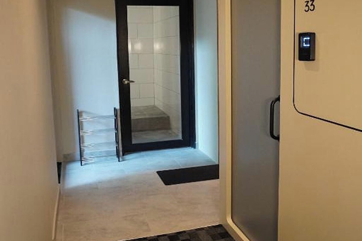 Un pasillo estrecho con una puerta marcada '33', una cámara de seguridad y una puerta de cristal que da a una habitación.