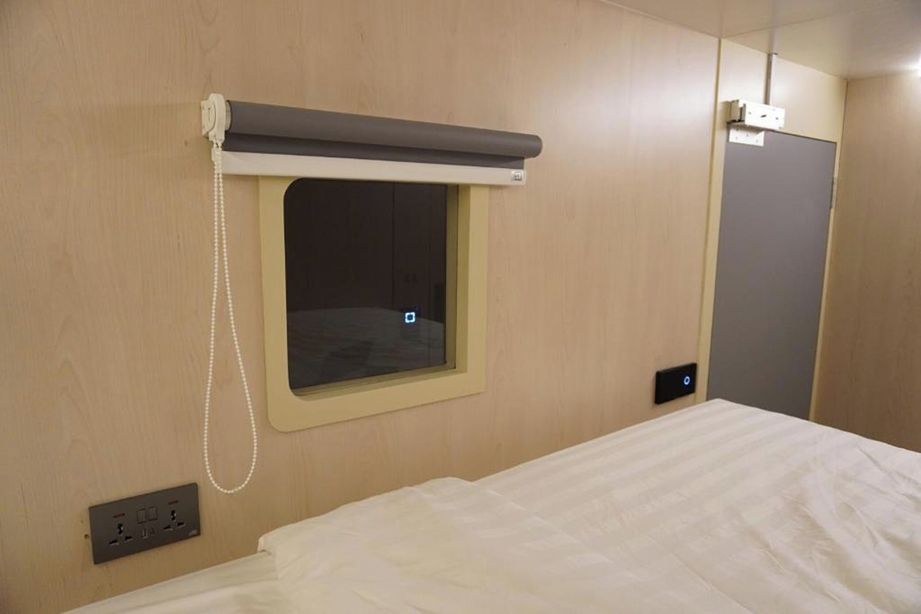 Une chambre d’hôtel avec un lit, une fenêtre avec un rideau, une prise électrique et une porte.