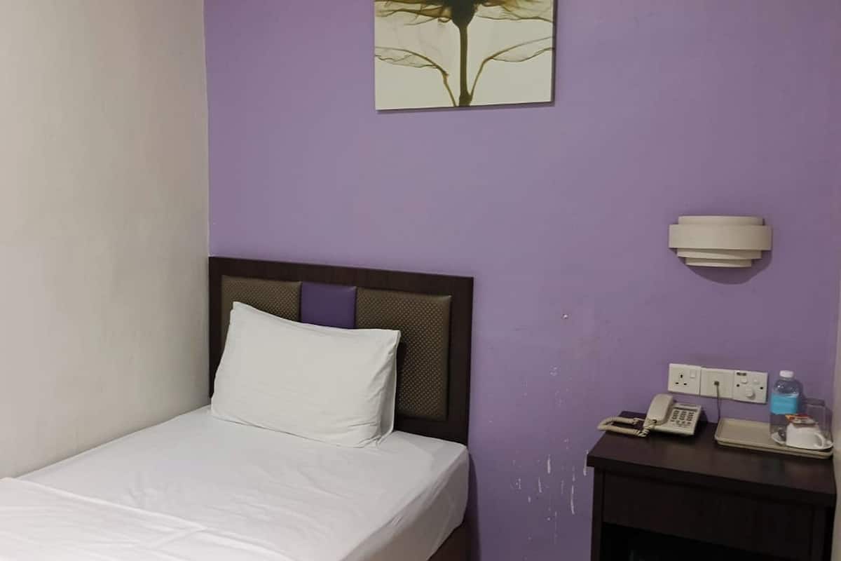 A hotel room with a bed, a nightstand with a phone and a bottle, and a wall-mounted light fixture.
