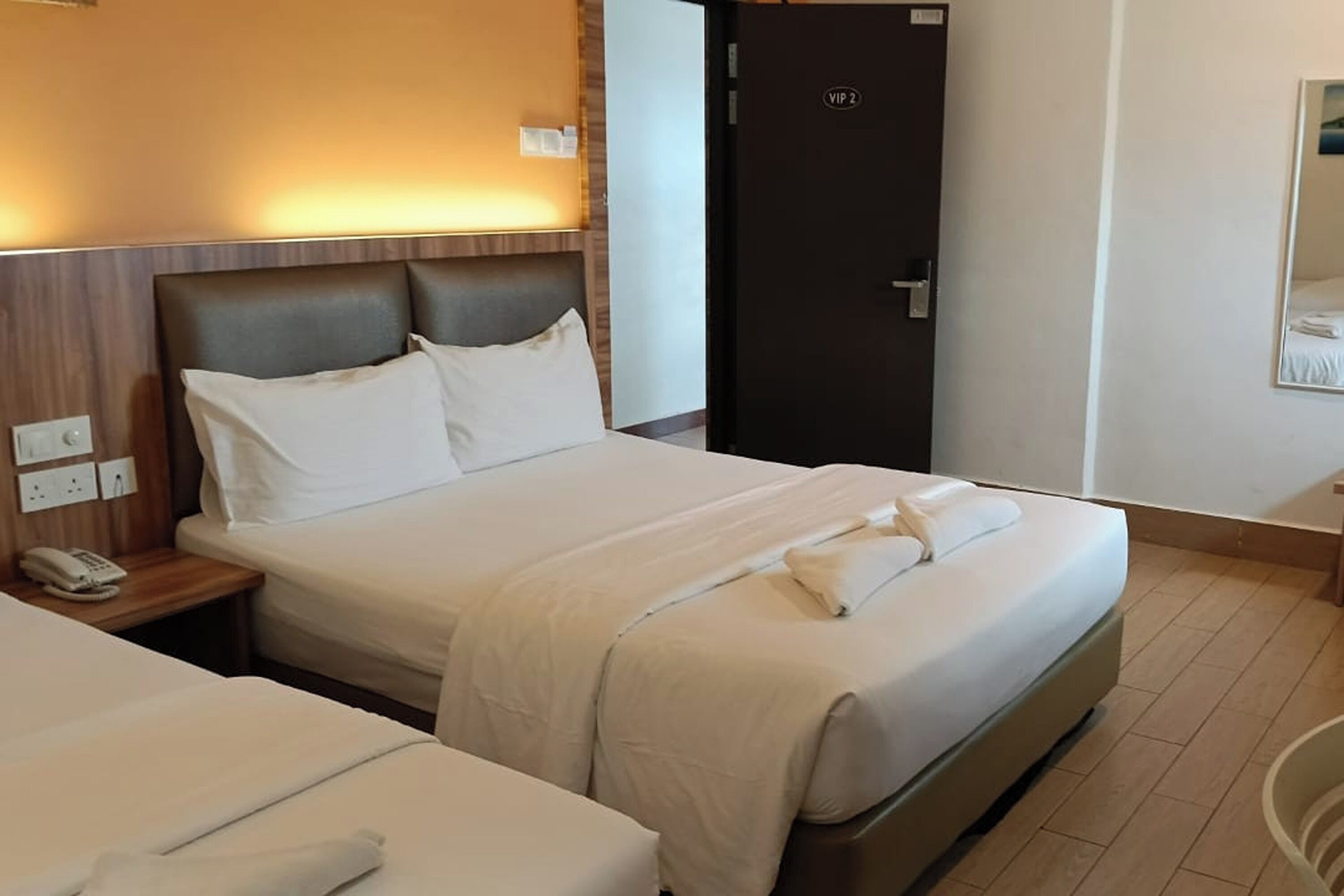 A hotel room with two beds, a wooden headboard, a bedside phone, and a door marked "VIP 2".