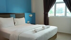 A neatly made bed in a hotel room with a blue accent wall, a window with curtains, and a visible power outlet on the nightstand. - Hotel City 88 Sdn Bhd [Batu Pahat] (Batu Pahat)