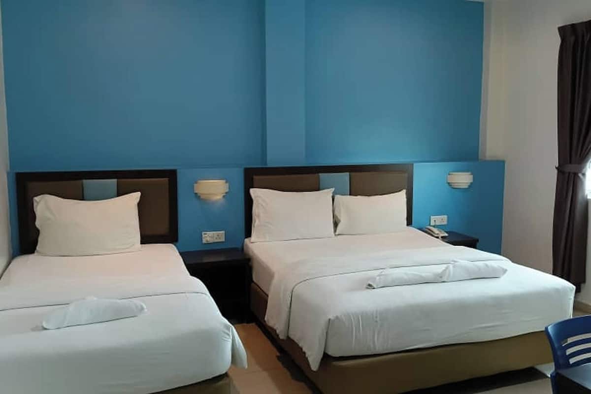 A hotel room with two beds, each with white bedding and headboards. There are bedside tables with lamps and a phone on one of them. The walls are painted blue, and there is a window with curtains.