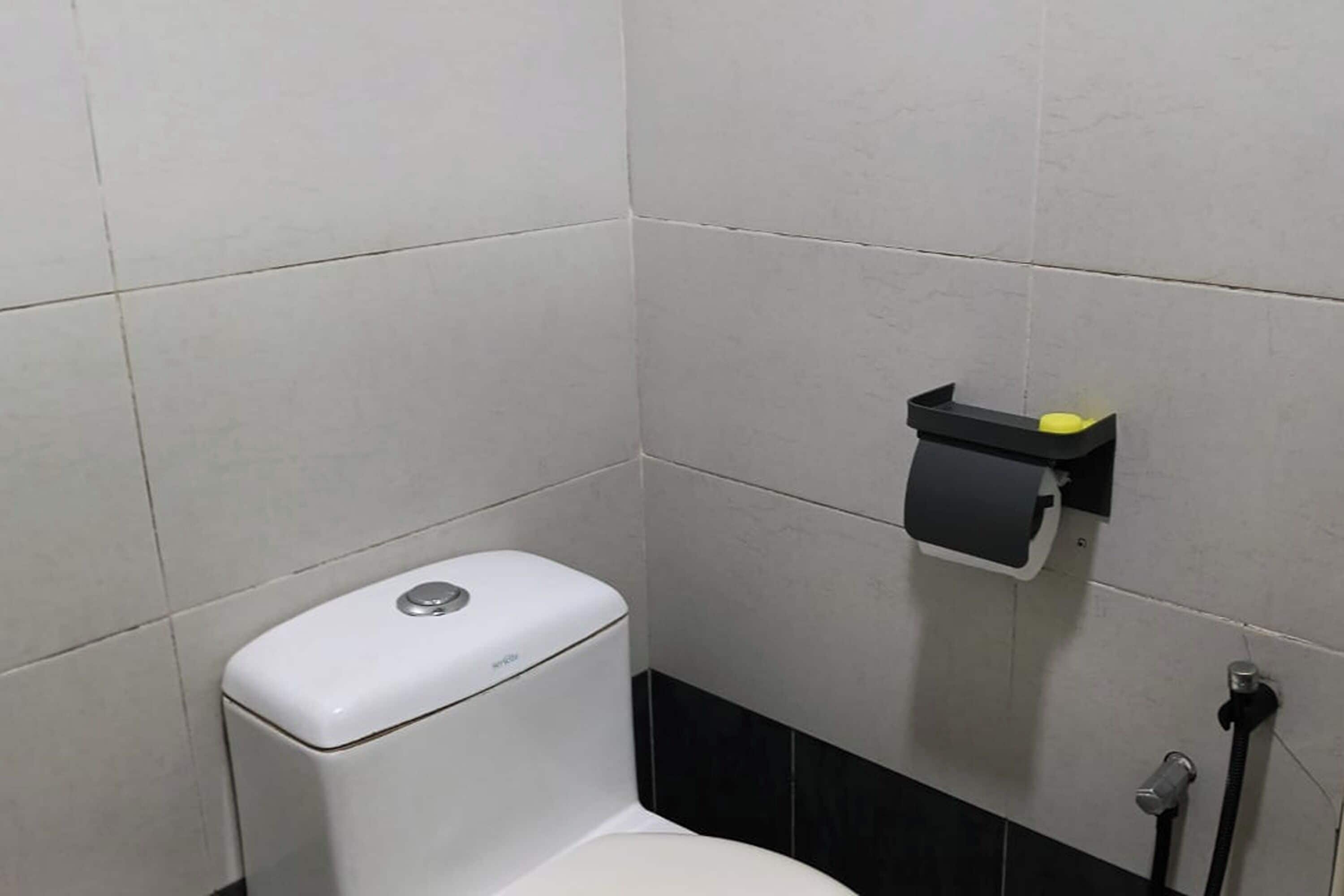A corner of a bathroom with a white toilet, a black and white tiled wall, and a small black shelf with a yellow object on it.