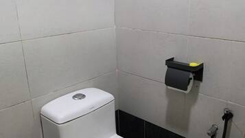 A corner of a bathroom with a white toilet, a black and white tiled wall, and a small black shelf with a yellow object on it.