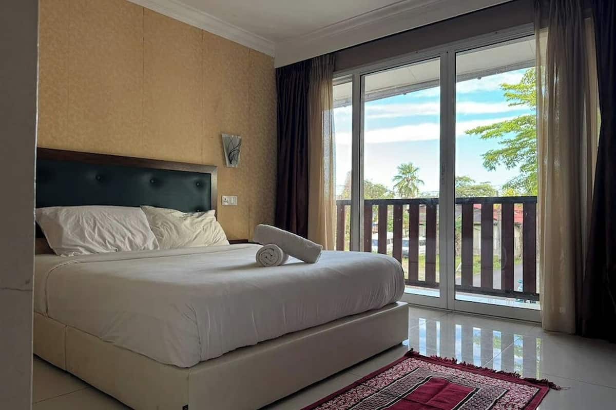 Una camera d'albergo con un letto grande, una testiera, una finestra che offre vista sull'esterno e un tappeto rosso sul pavimento.