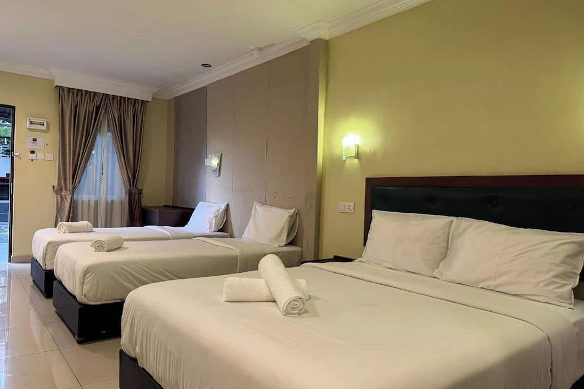 Una camera d'albergo con due letti, entrambi con lenzuola bianche e asciugamani arrotolati. Tra i letti si trova un comodino, una lampada a parete e una finestra con tende.