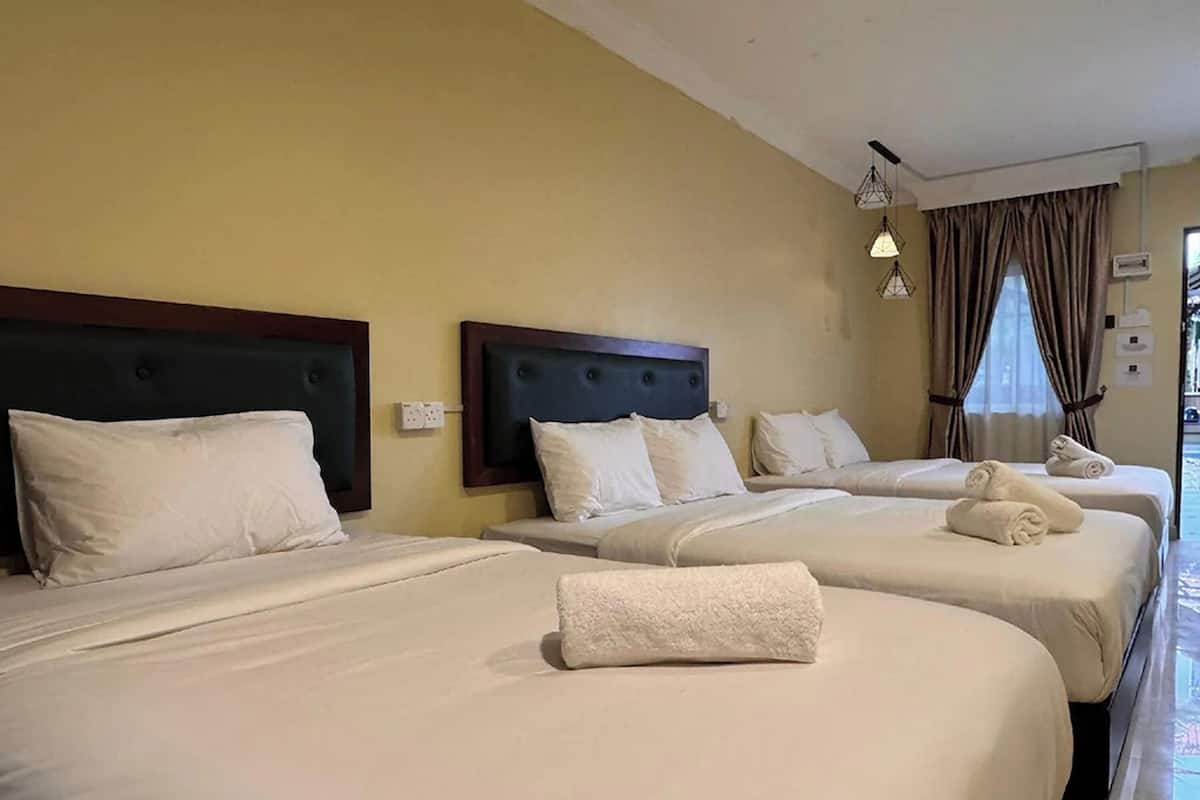 Camera d'albergo con tre letti, ognuno dotato di una testata scura e biancheria bianca. Sono presenti due lampade da comodino e una finestra con tende.