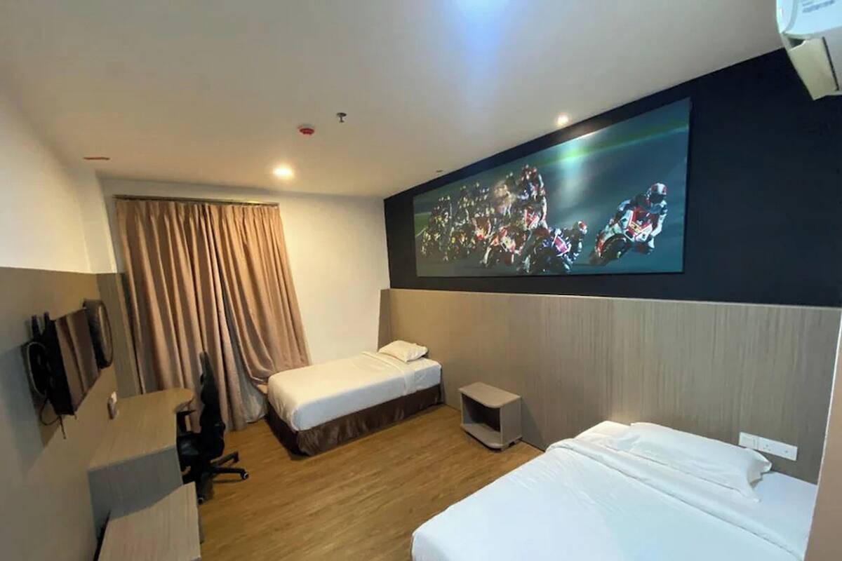 Ein Hotelzimmer mit zwei Betten, einem an der Wand montierten Fernseher, einem Schreibtisch und einem Sessel.