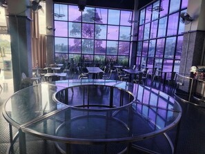 A modern restaurant with round tables and chairs, large windows with a view of trees and a purple sky. - Arafah Hotel Nilai (Nilai)