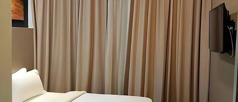 Una habitación de hotel con una cama, cortinas y un televisor montado en la pared.