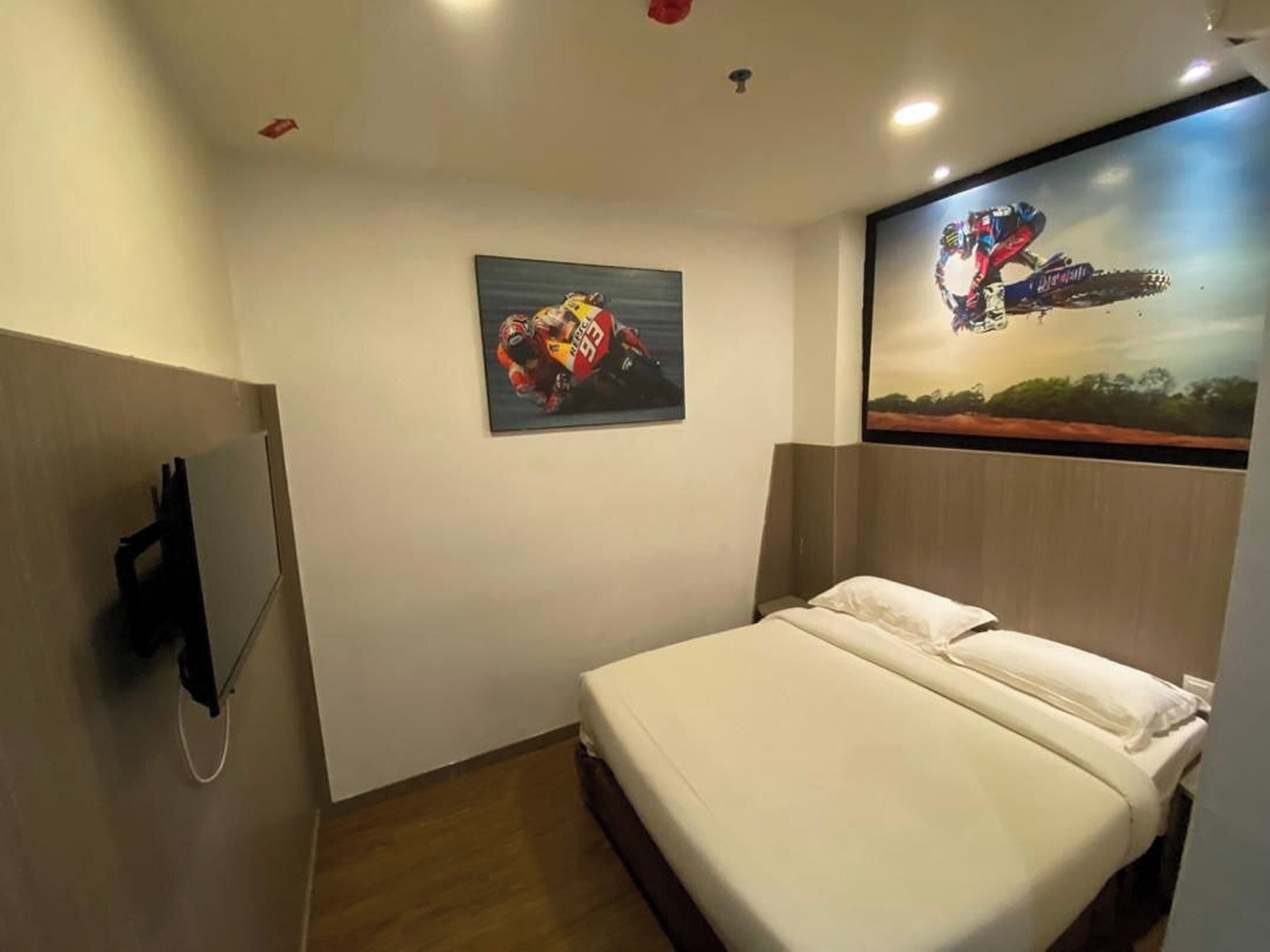 Una habitación de hotel con cama, televisor montado y dos cuadros colgados en la pared.