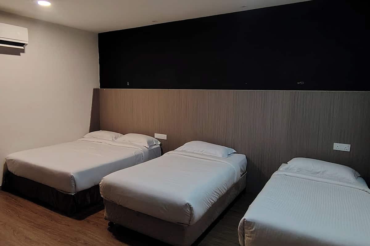Ein Hotelzimmer mit drei Einzelbetten, einem Holzkopfende, einer weißen Klimaanlage und einer schlichten Wand.