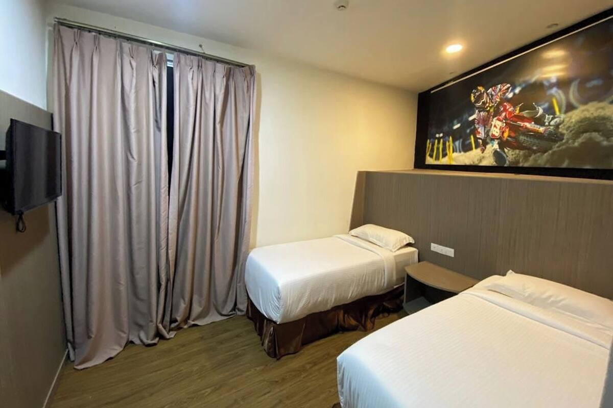 Ein Hotelzimmer mit zwei Einzelbetten, einem an der Wand montierten Fernseher und einem großen Fenster mit Vorhängen.