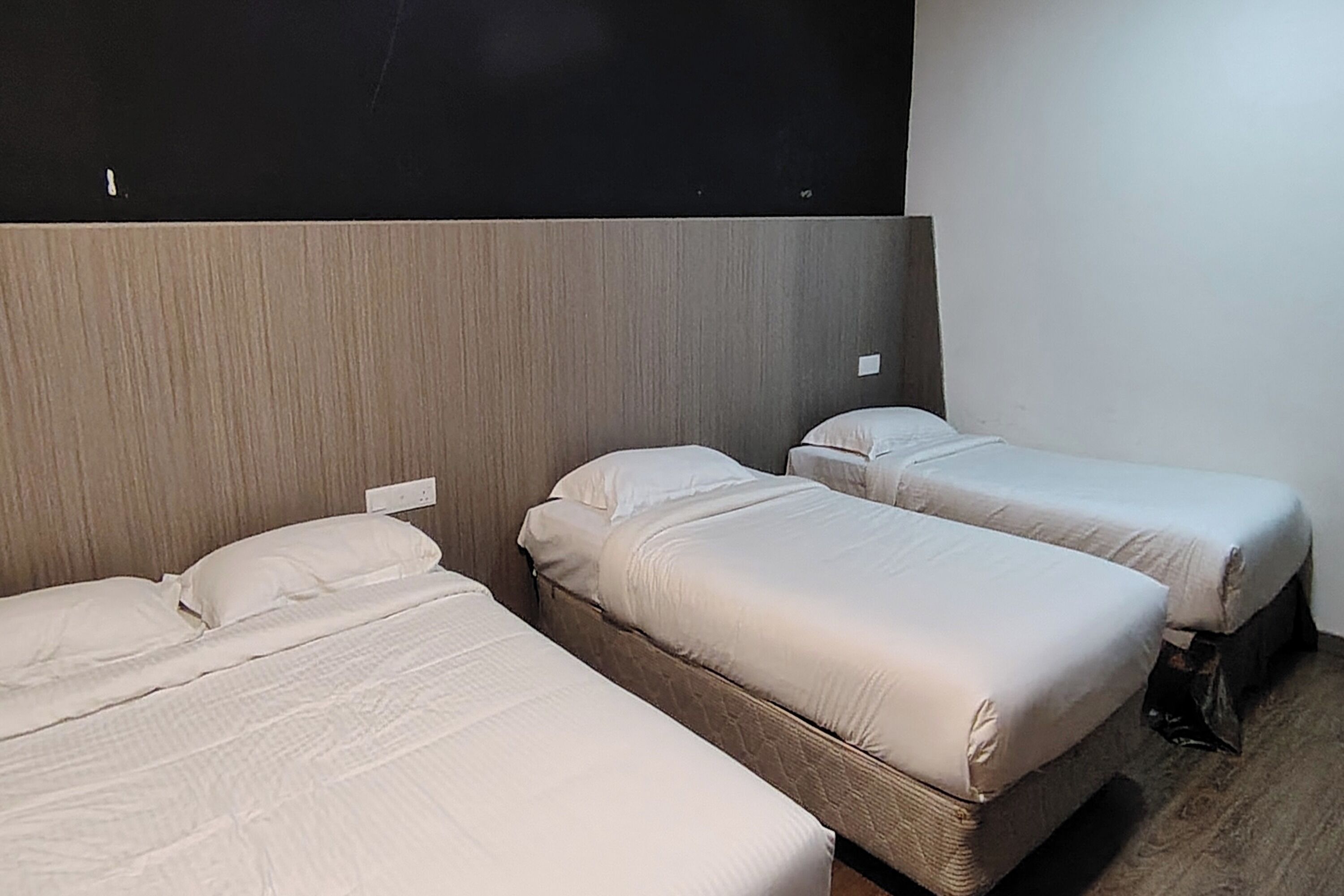 A room with three single beds, a dark headboard, and a wooden floor.