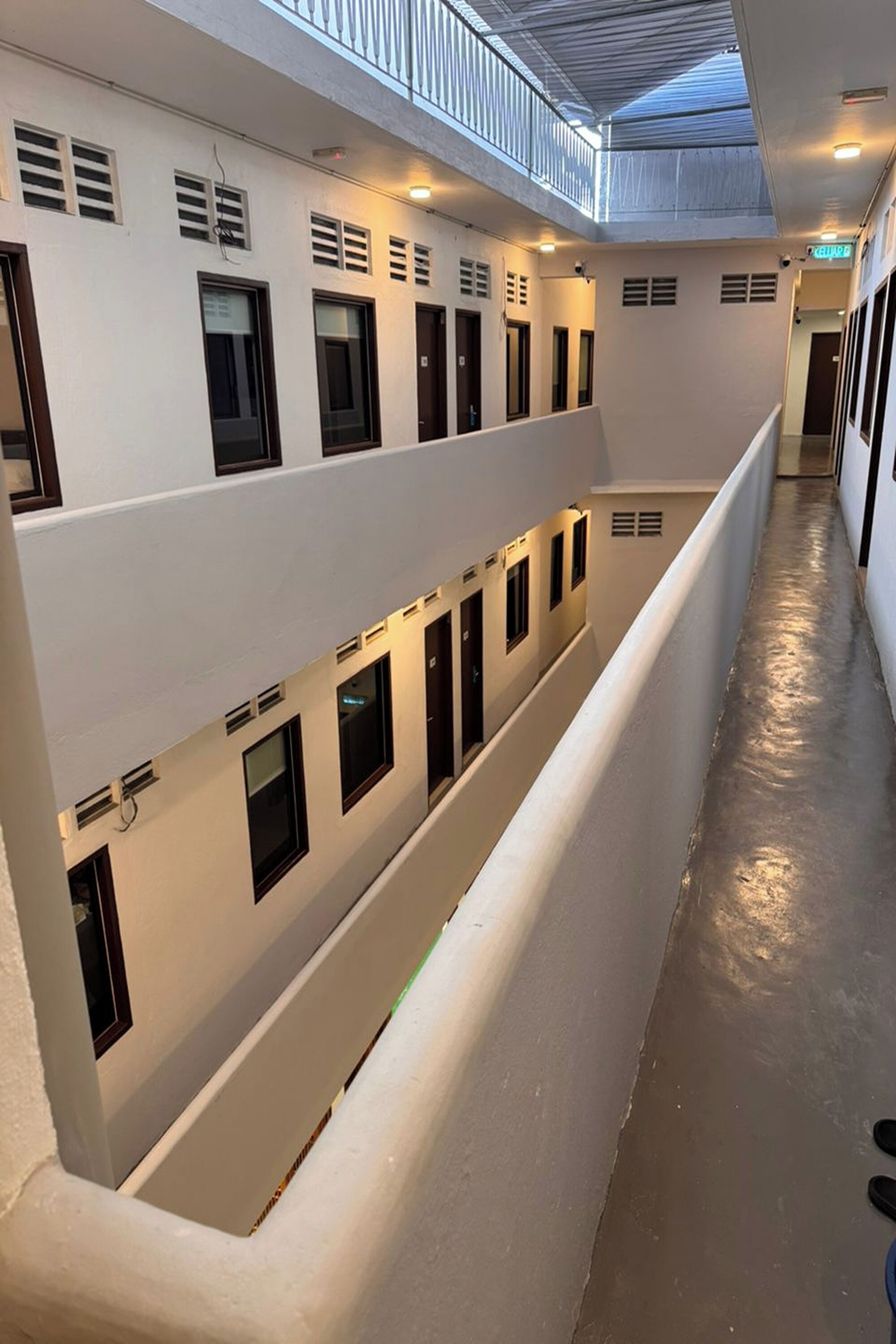 A multi-level corridor with a central walkway, white walls, and small windows.
