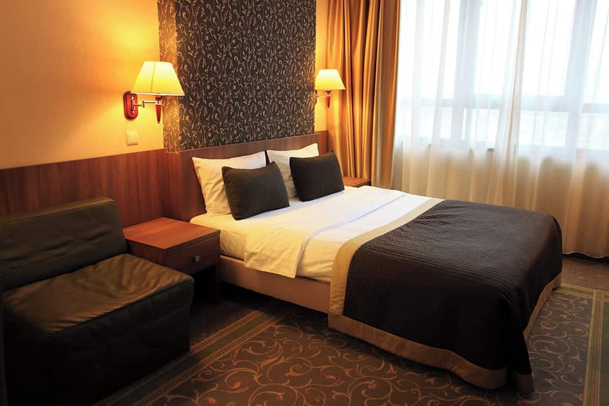 Habitación de hotel con cama, dos lámparas de noche, mesita de noche, sofá y alfombra estampada.