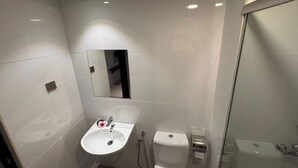 Un baño moderno con lavamanos blanco, espejo y cabina de ducha de vidrio.
