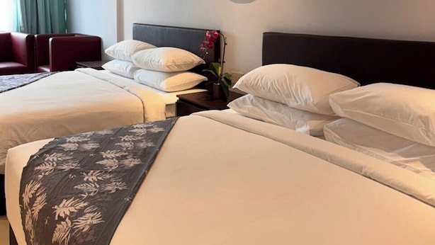 Habitación de hotel con dos camas, un adorno en la pared, aire acondicionado en el techo y una ventana con cortinas.