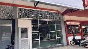 Fachada de tienda con vidrio, un panel decorativo metálico sobre la entrada y una motocicleta estacionada a la derecha.
