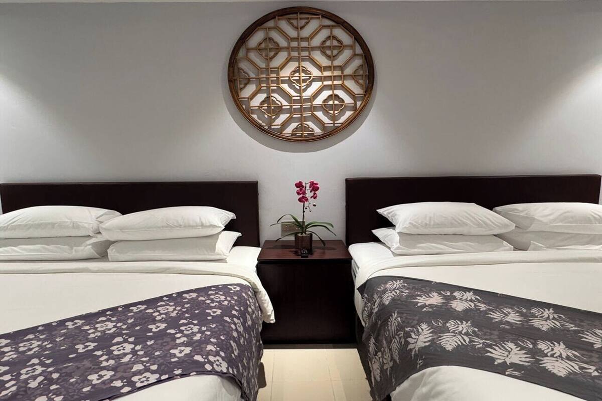 Habitación de hotel con dos camas, un panel decorativo en la pared y una mesita con una planta en maceta.
