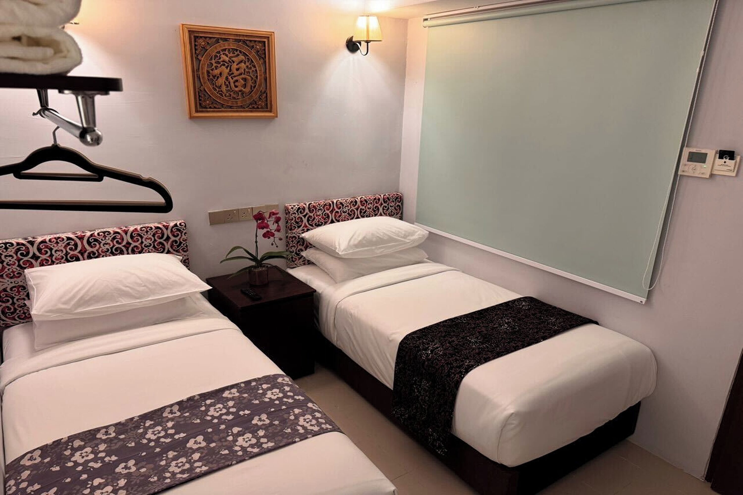 A hotel room with two beds, a nightstand, a wall-mounted lamp, and a decorative wall piece.