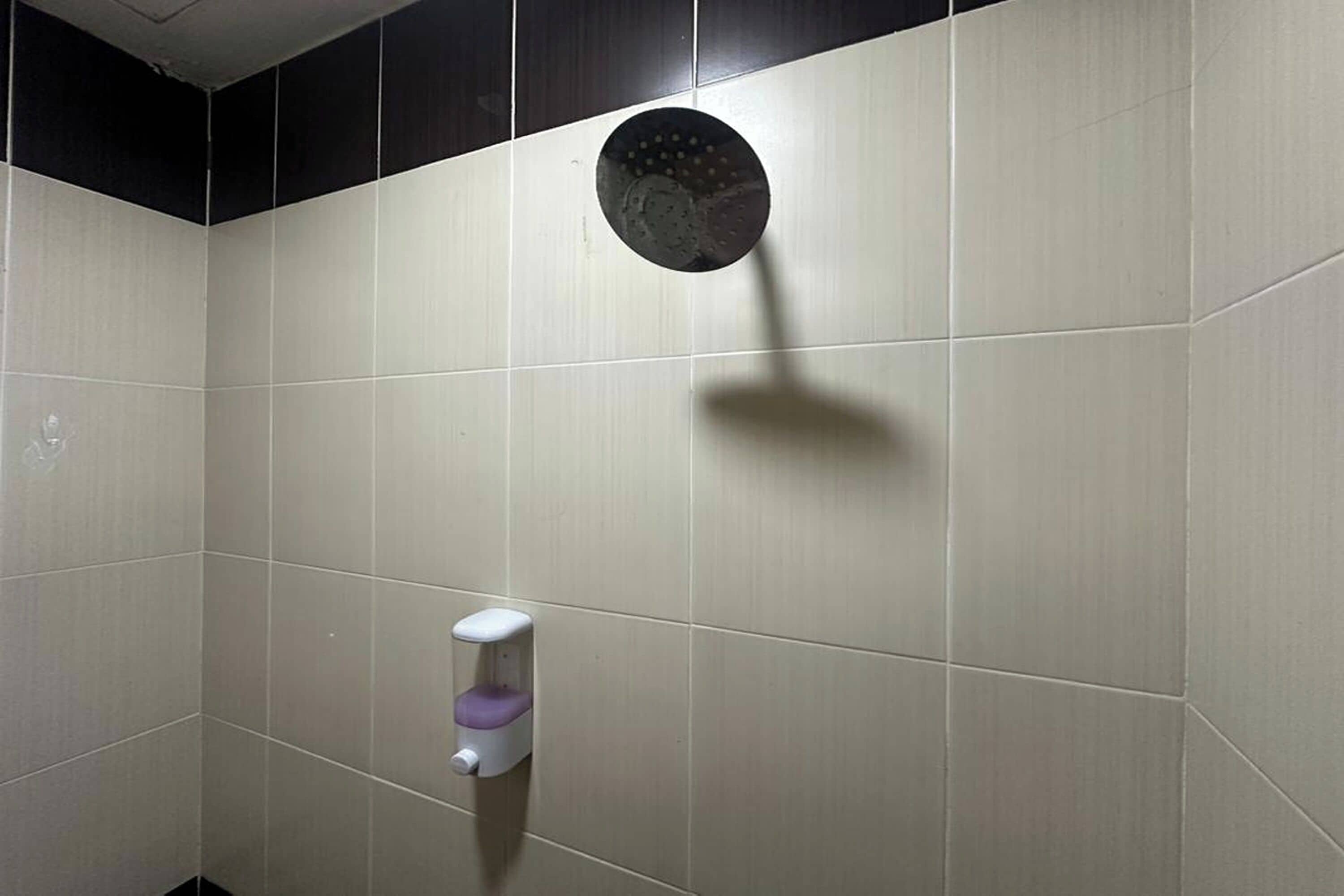 A bathroom with a hand dryer and a showerhead on the wall.