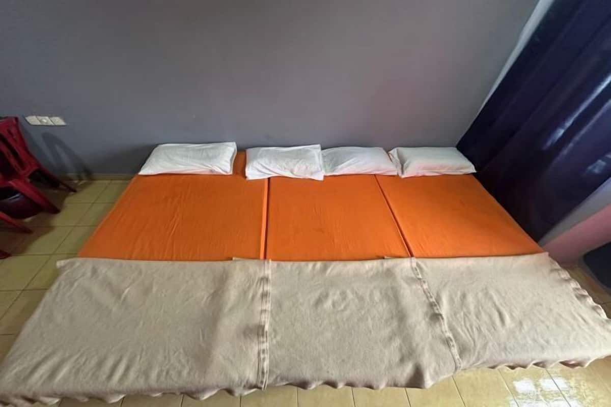 Una cama con una colcha anaranjada y beige, almohadas blancas y una silla roja en la esquina.