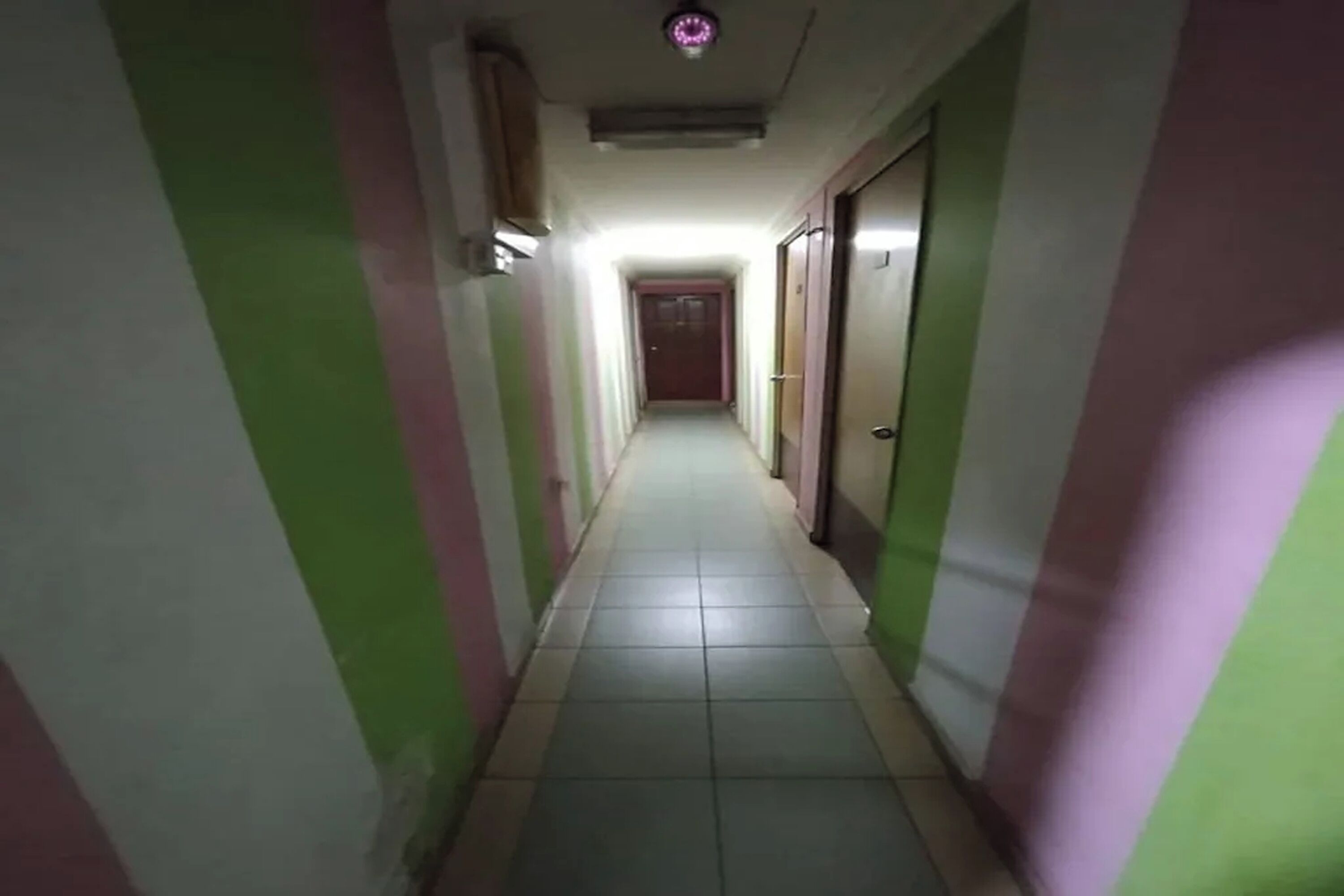 A narrow hallway with green and pink walls, a tiled floor, and doors on both sides.