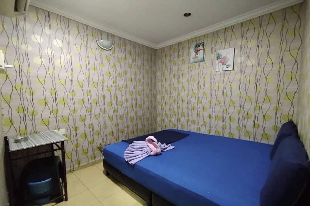 Una habitación pequeña con cama individual, colchón azul, una mesita con silla y papel tapiz estampado.