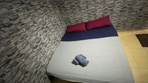 Ein Bett mit gestreifter Bettdecke, zwei Kissen und ein gefaltetes Handtuch in einem Raum mit Steinwänden und Fliesenboden.