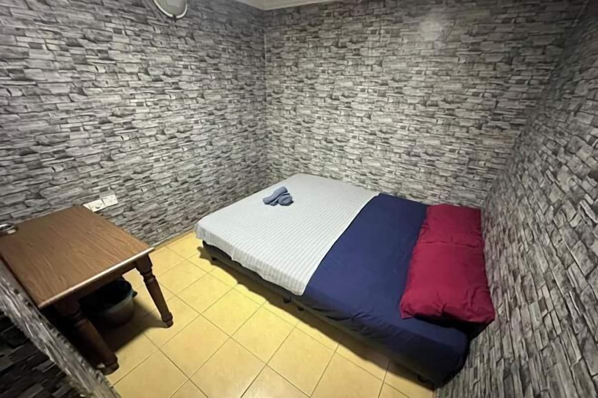 Una habitación pequeña con una cama, una mesa de madera y una pared con diseño de piedra.