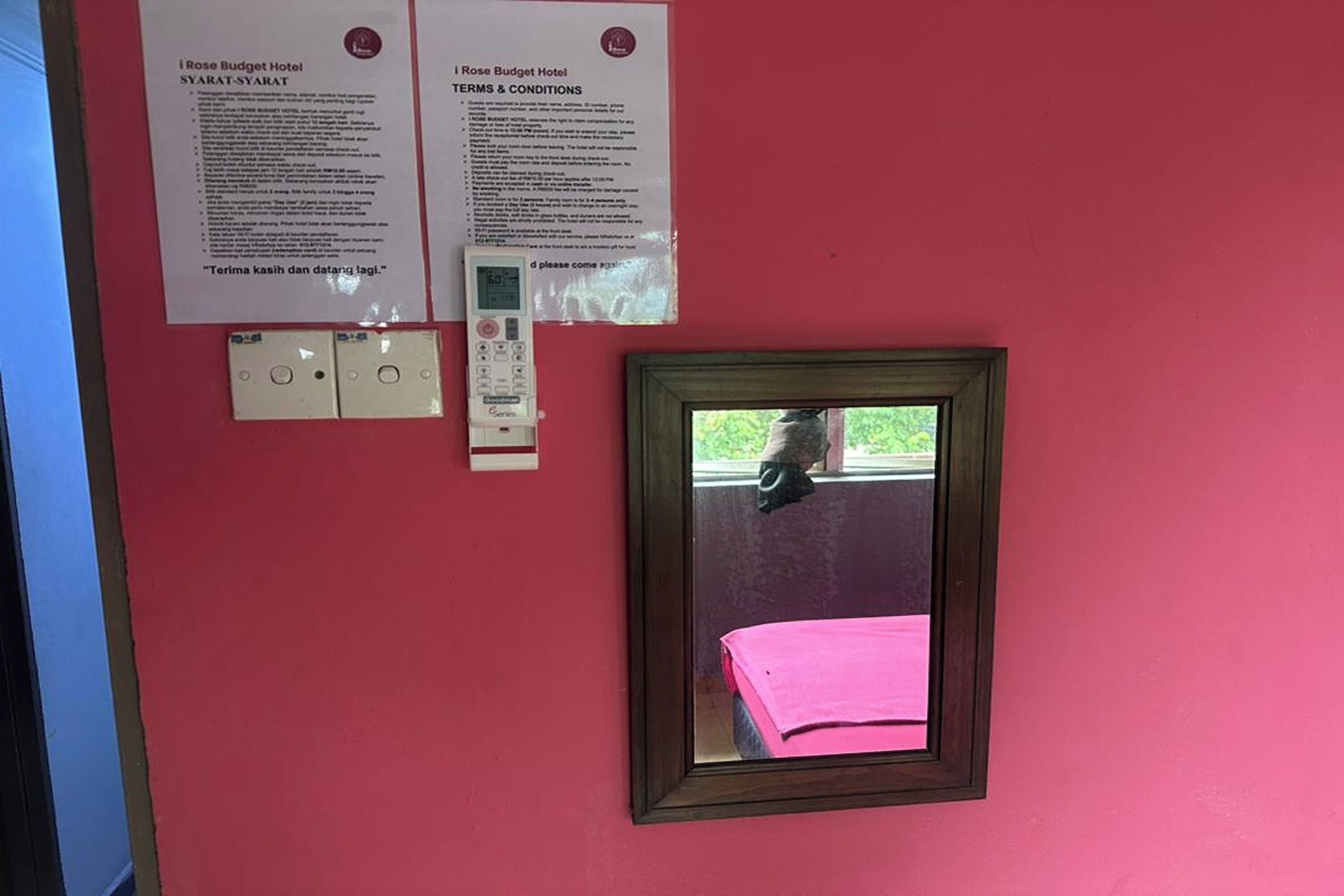 Una habitación con una pared roja, un cuadro enmarcado y dos carteles informativos.