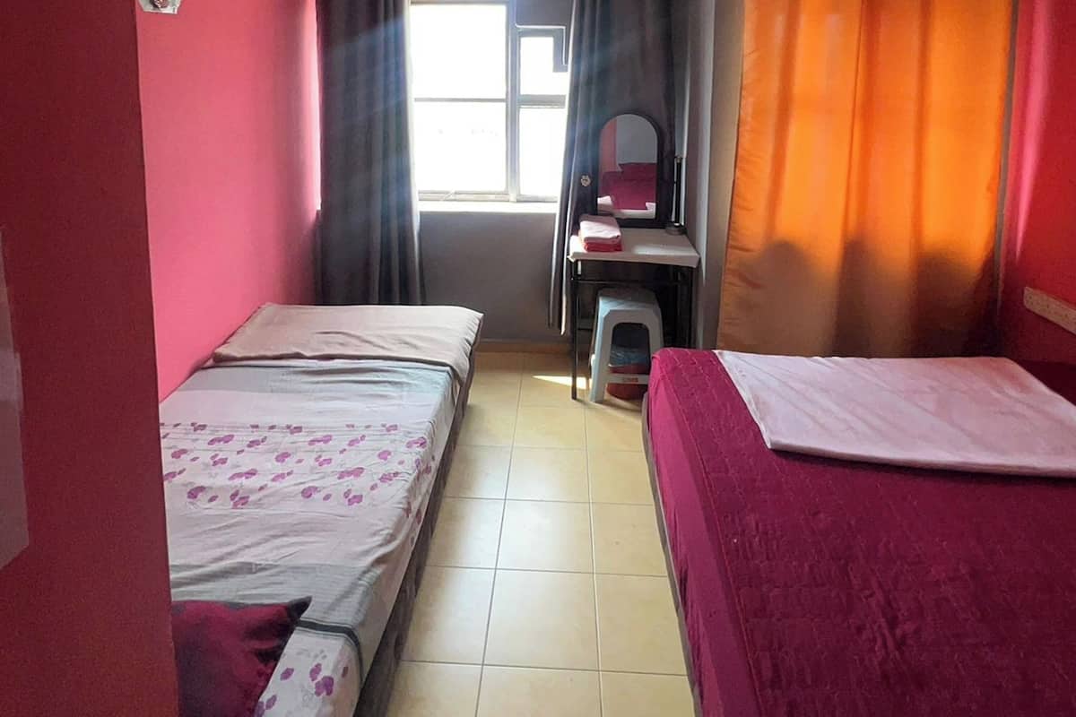 Una habitación con dos camas, una mesita con espejo y una ventana con cortinas.