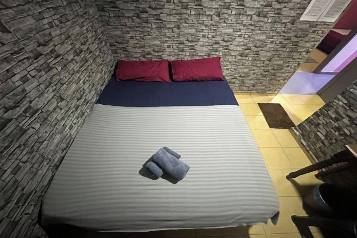 A narrow room with a bed, stone walls, and a small table.