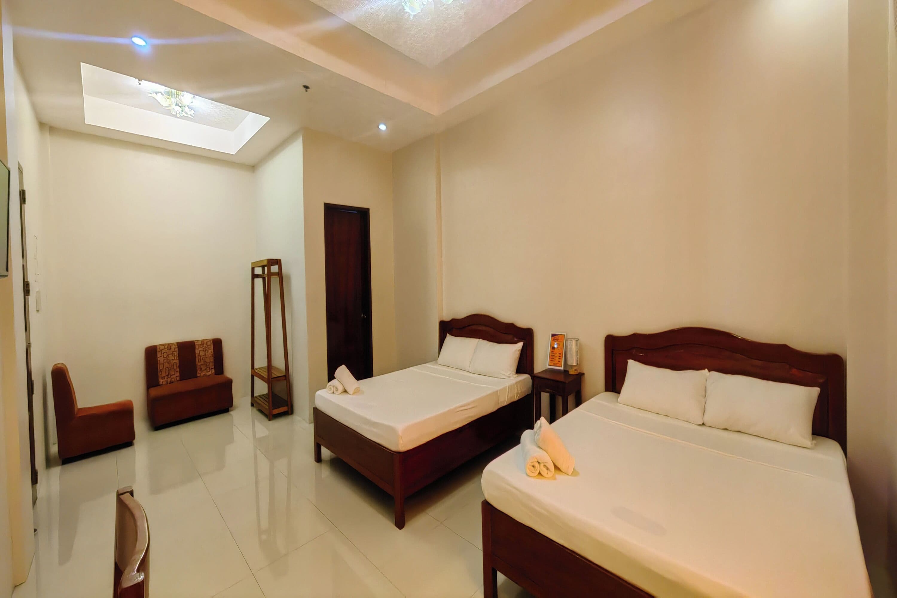A hotel room with two beds, a sofa, a bedside table, and a ceiling light.