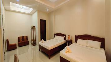 A hotel room with two beds, a sofa, a bedside table, and a ceiling light.