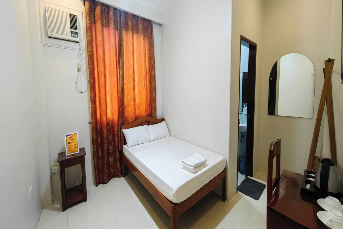 A neatly made bed with white linens, a wooden headboard, a small bedside table with a menu, and a mirror on the wall.