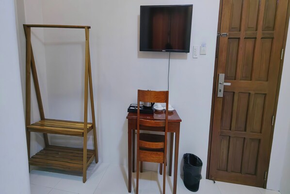 A room with a wooden chair, a small wooden table with a television mounted on the wall, and a wooden door. - Isabelle Hotel (Puerto Princesa)