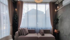 A modern living room with a sectional sofa, large windows with sheer curtains, and a chandelier. - Isabelle Hotel (Puerto Princesa)