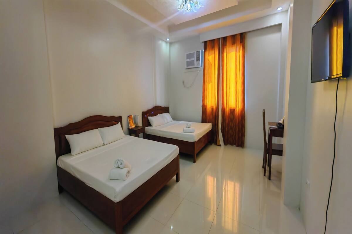 A hotel room with two beds, a desk, a chair, and a TV.
