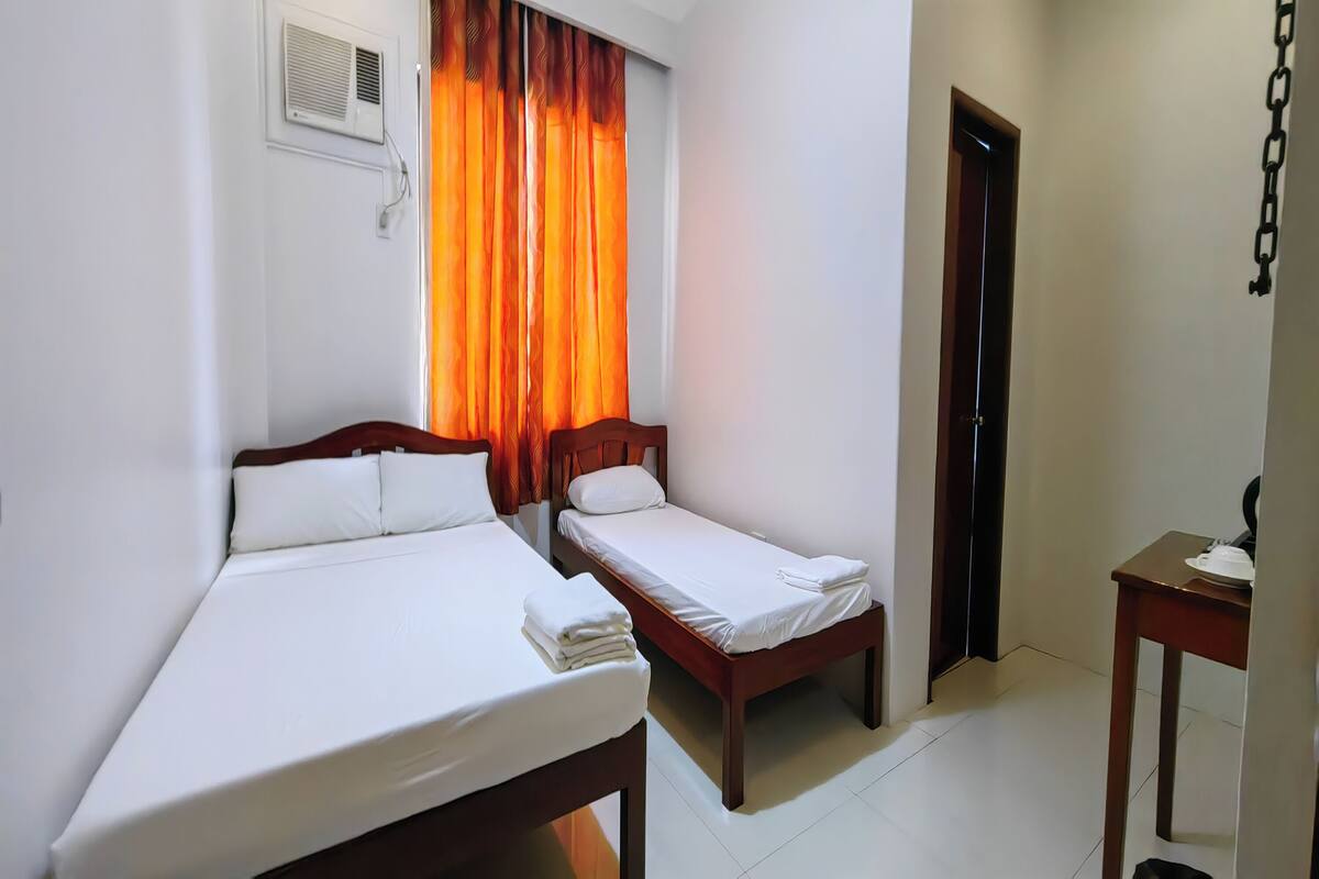 A hotel room with two beds, a wooden headboard, a small table, and an air conditioning unit on the wall.
