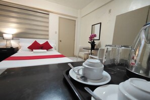 A hotel room with a bed, a dining table with white cups and saucers, a small table with a vase of flowers, and a mirror on the wall. - Orangenest Apartelle (Manila)