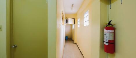 A narrow hallway with a fire extinguisher mounted on the wall, a door on the left, and a window on the right.