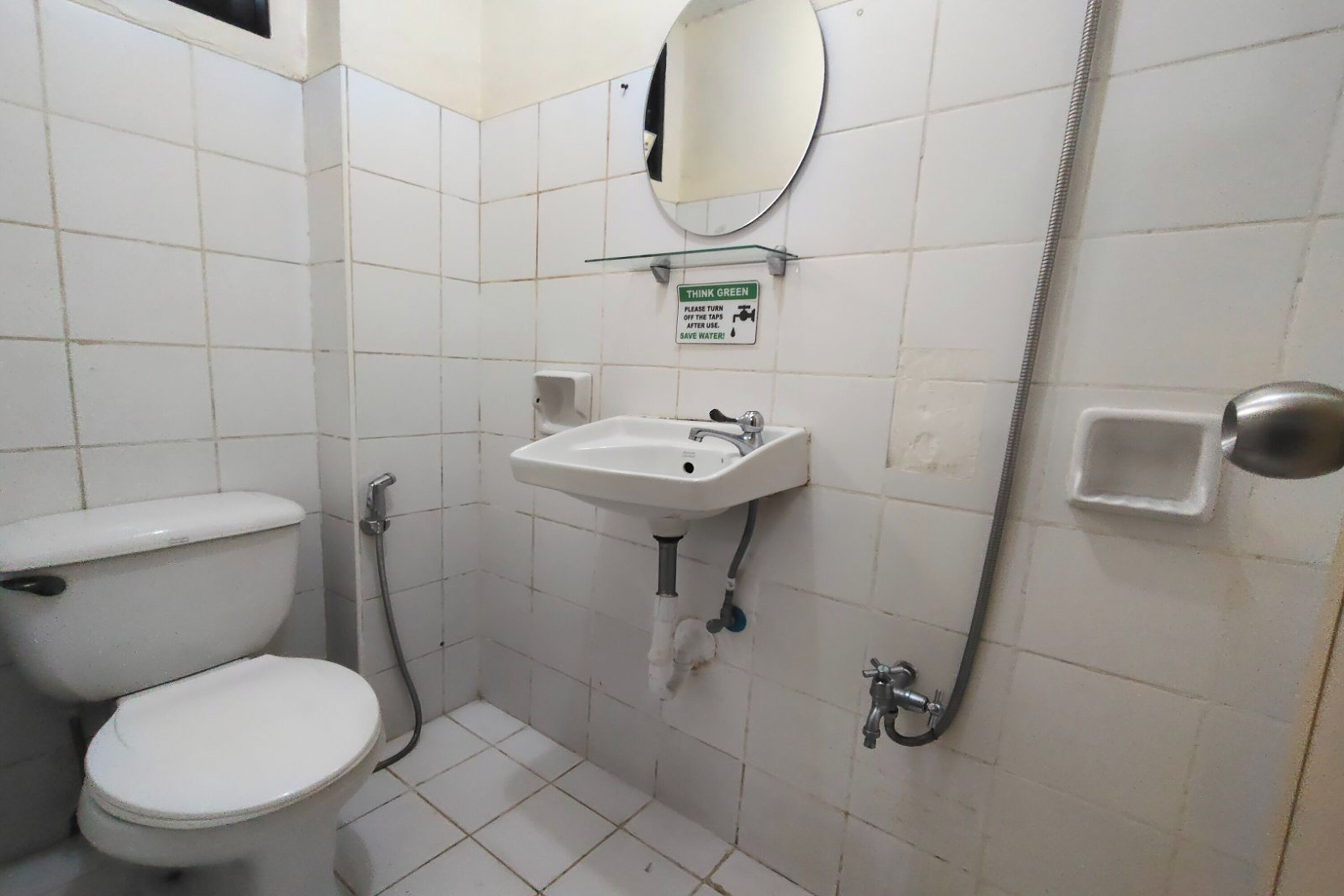 Un baño pequeño y limpio con inodoro, lavabo y ducha. Un cartel sobre el lavabo indica ahorrar agua y ser ecológicos.