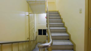 Egy keskeny lépcső, melynek fém korlátja és kapaszkodója van, és egy felső szintre vezet.