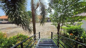Un escalier mène à un espace extérieur abrité, agrémenté de palmiers, d’où l’on aperçoit un bâtiment au loin.